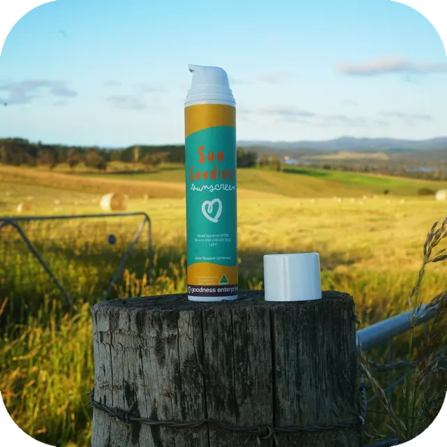 Sun Goodies Base Formula SPF 50 sunscreen bottle on a timber fence post above a hay field