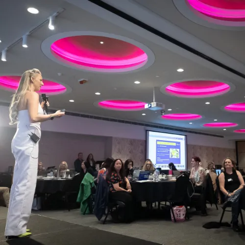 Sarah Cordiner presenting to a large room under pink lights