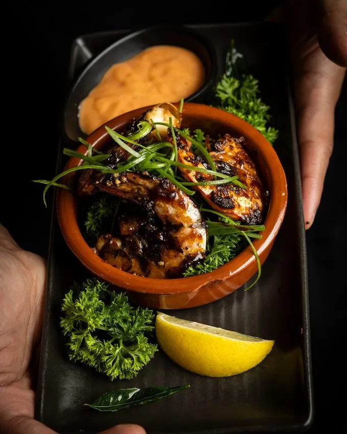 Grilled prawns in a clay bowl with fresh herbs and lemon