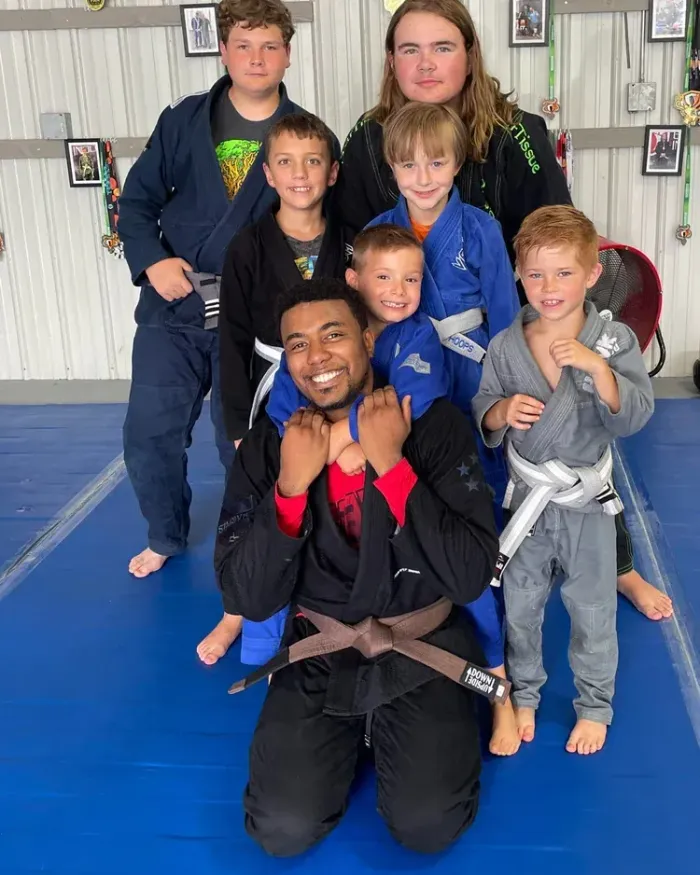 Coach Brandon Williams with a group of smiling kids on the mat at Delta