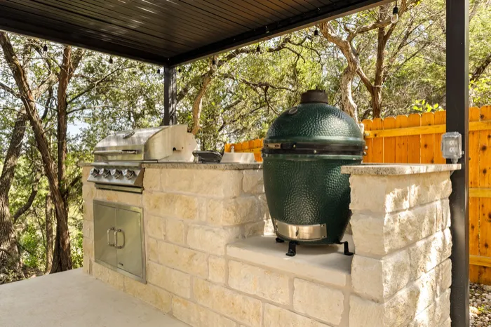 Outdoor kitchen in limestone with a grill and kamado under a steel roof, Wimberley