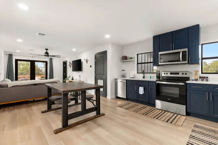 Open kitchen and dining with navy cabinets, stainless appliances and plank flooring