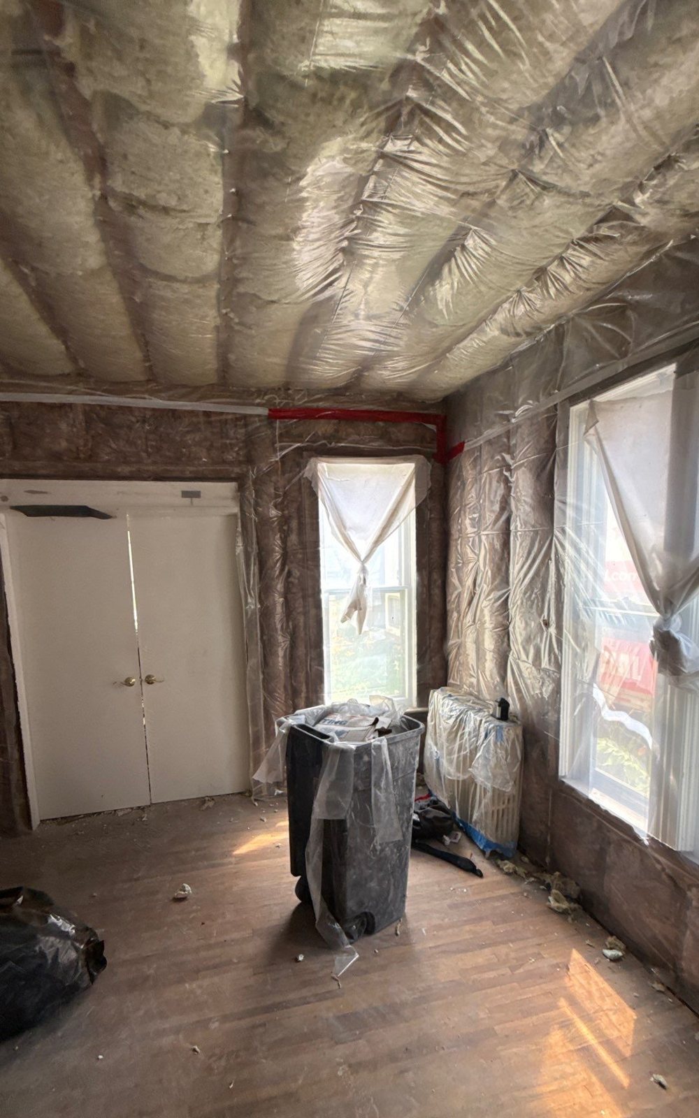 Rebuilt room with new stud walls and ceiling filled with insulation behind clear vapor barrier, bare wood floor