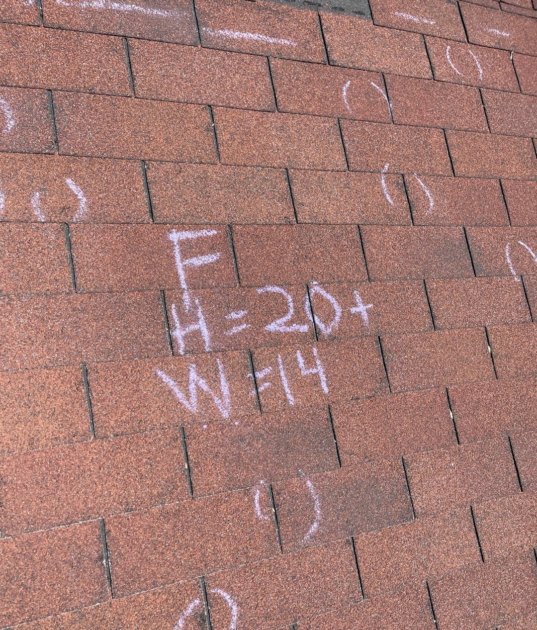 Asphalt shingles on a front roof slope with chalk circles around impacts and a tally reading H=20+ and W=14