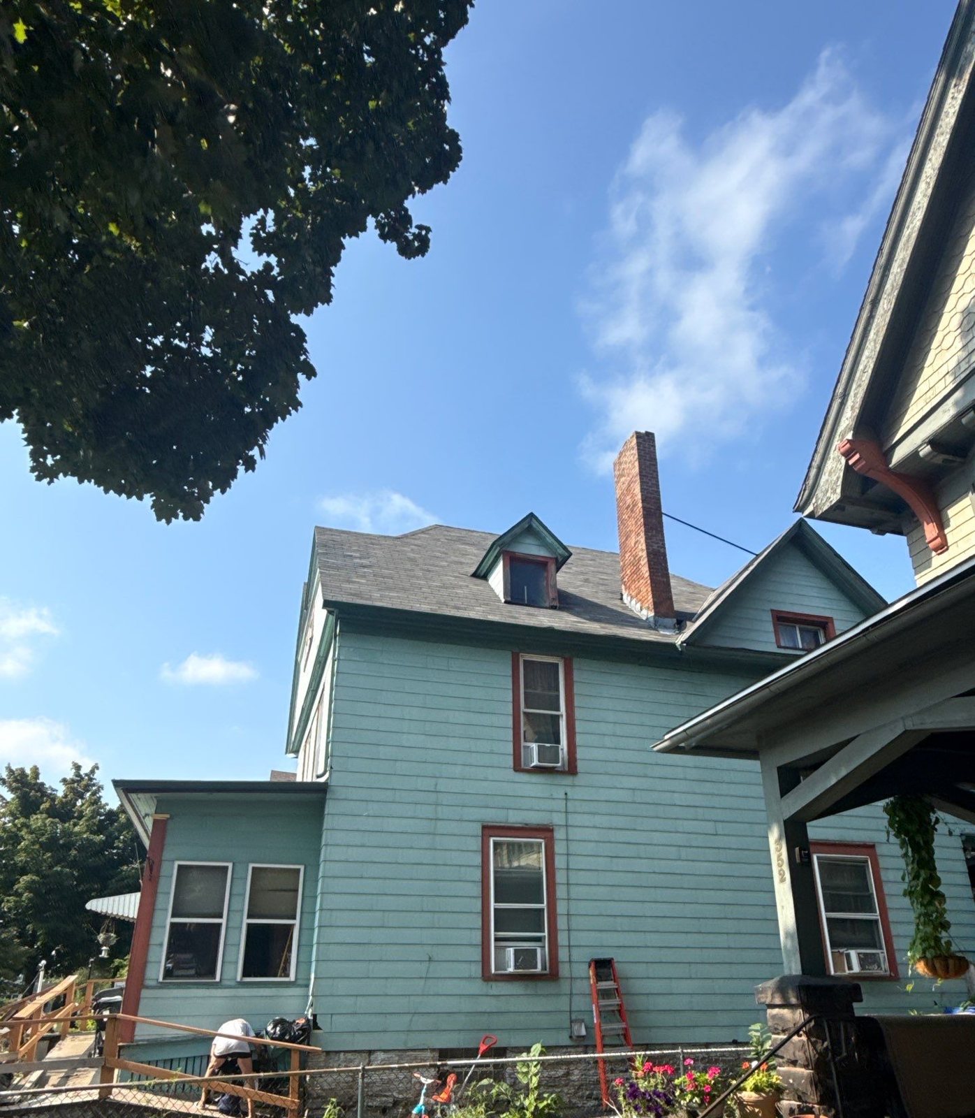 Older two-and-a-half-story Twin Cities house with steep dormers and a brick chimney, seen from the side yard