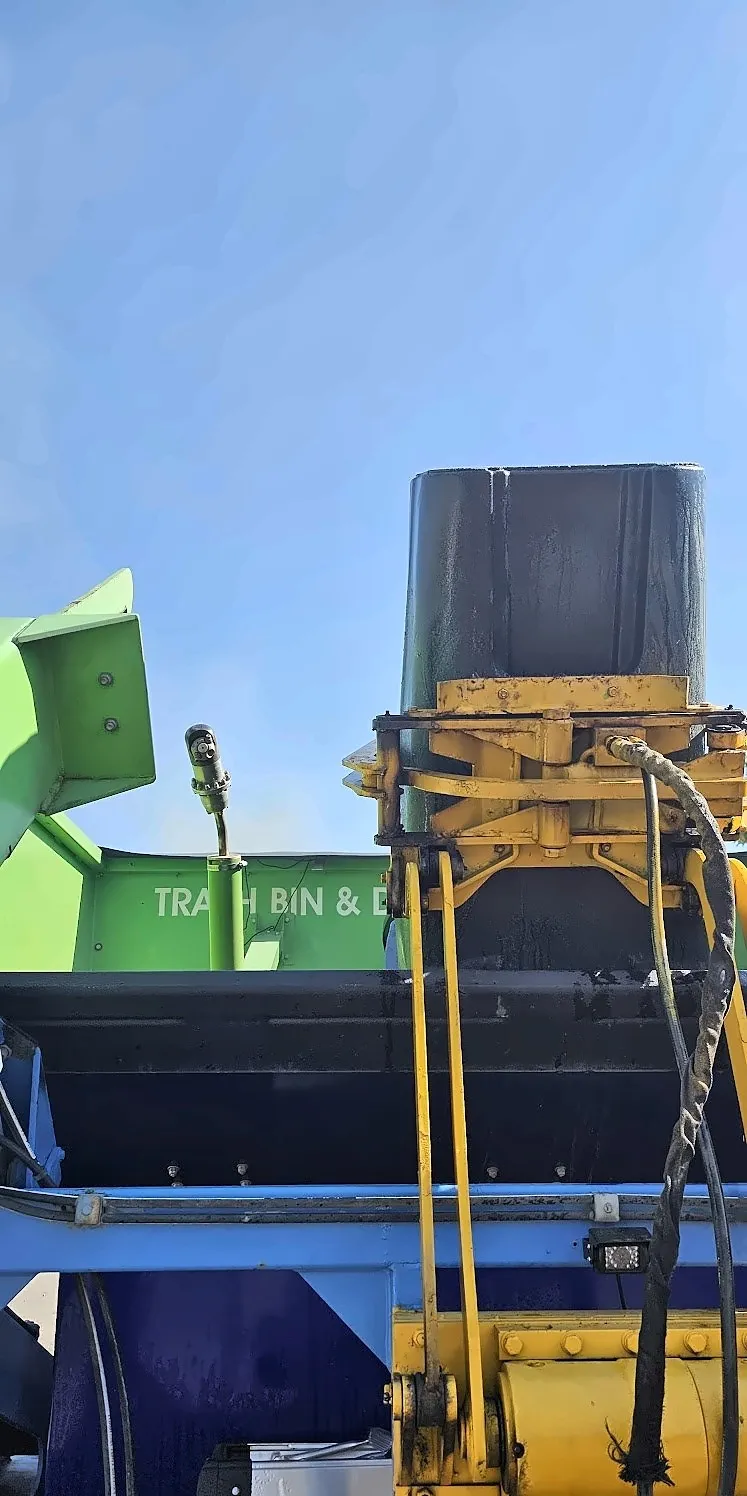 Close-up of the truck's hydraulic lift holding a trash bin over the washer
