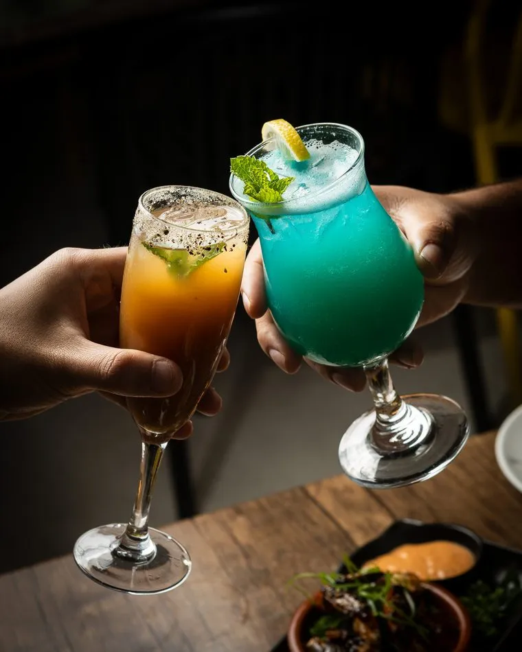 Two cocktails raised for a toast — an orange cocktail and a blue mocktail