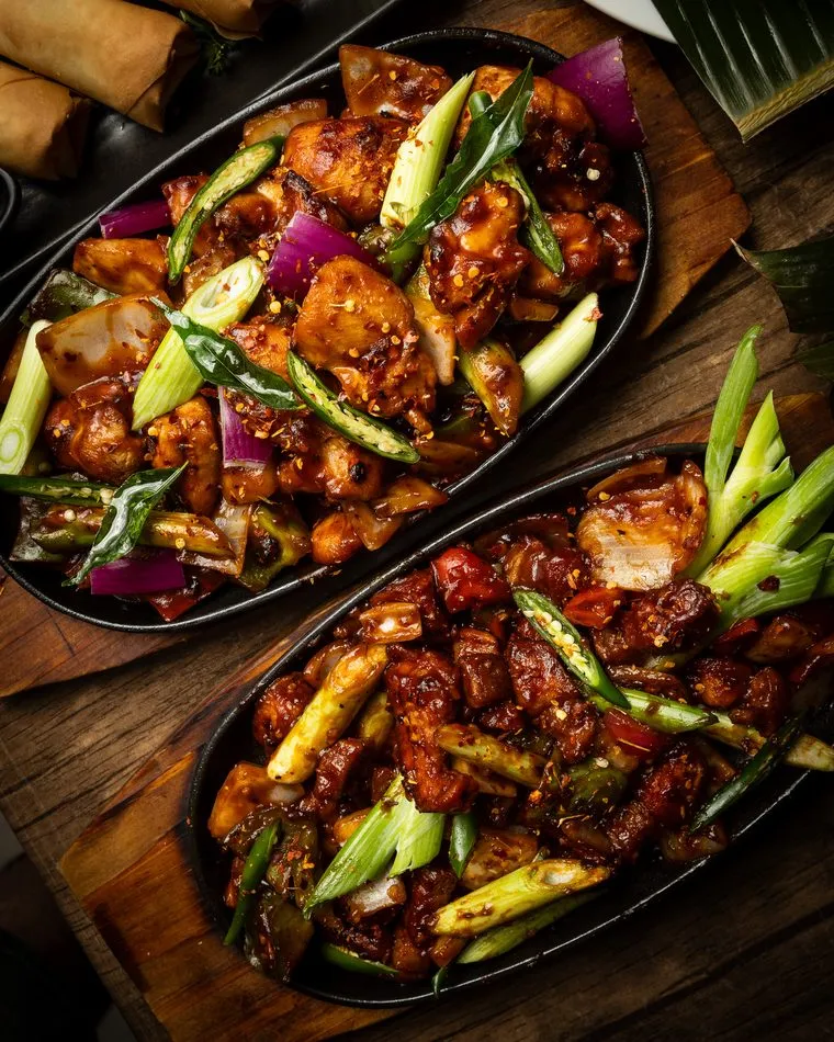 Two sizzling devilled dishes with capsicum, onion and spring onion on hot plates