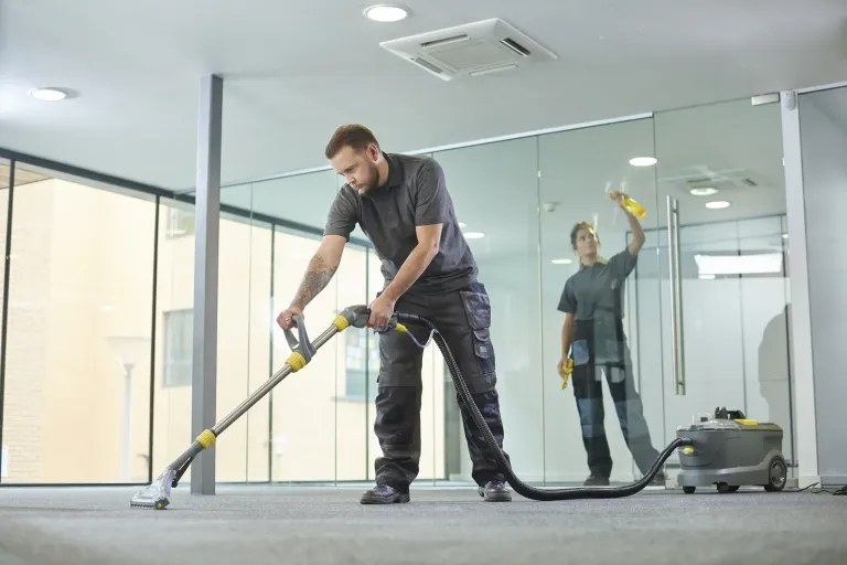 Technician running a floor cleaning machine in an office with glass walls