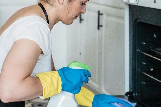 A cleaner wiping the inside of an oven while wearing protective gloves