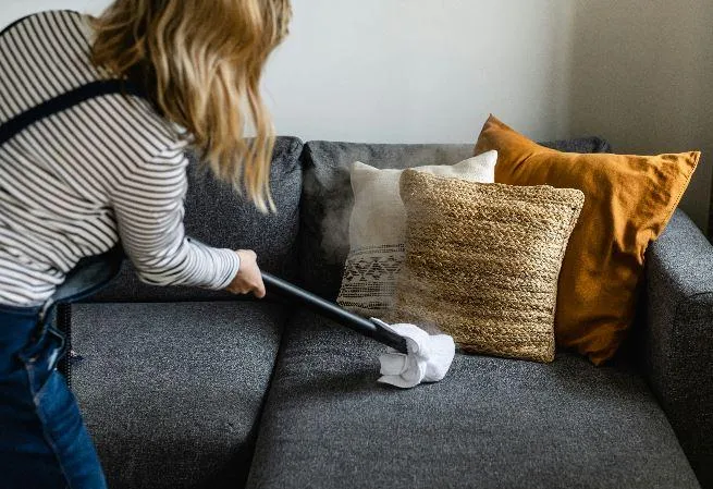 A cleaner vacuuming a gray sofa