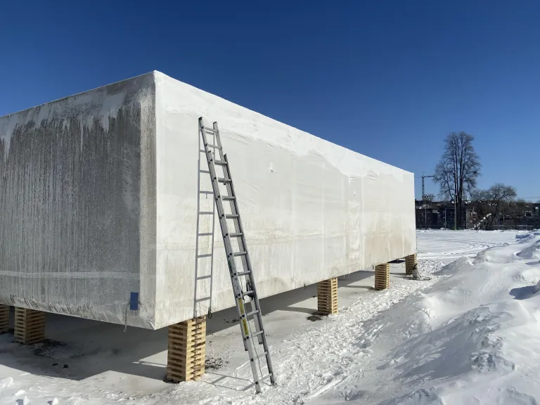 Large modular unit shrink wrapped in white film on timber cribbing outdoors in Ontario winter