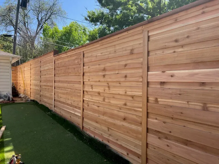 Tall horizontal cedar privacy fence along a side yard with artificial turf