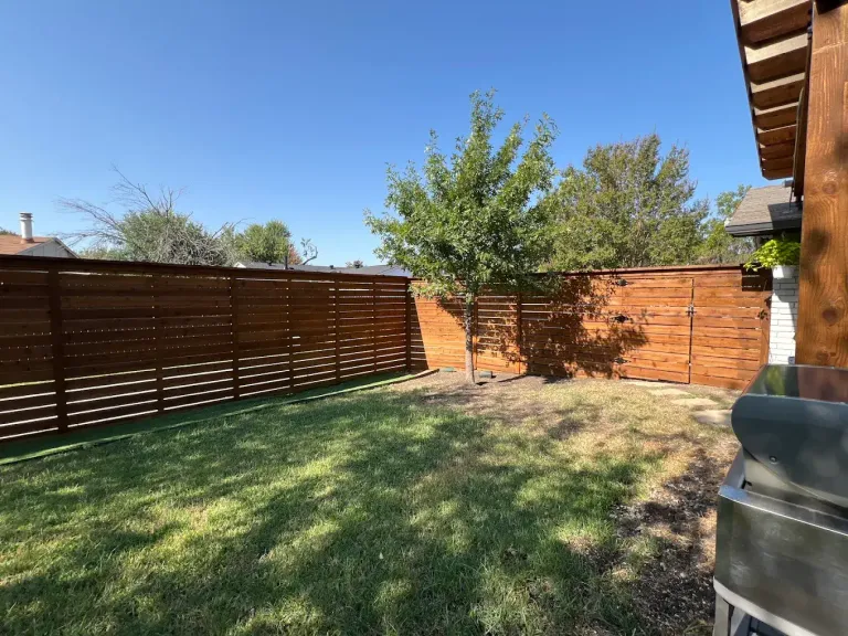 Long horizontal stained wood fence around a grassy backyard