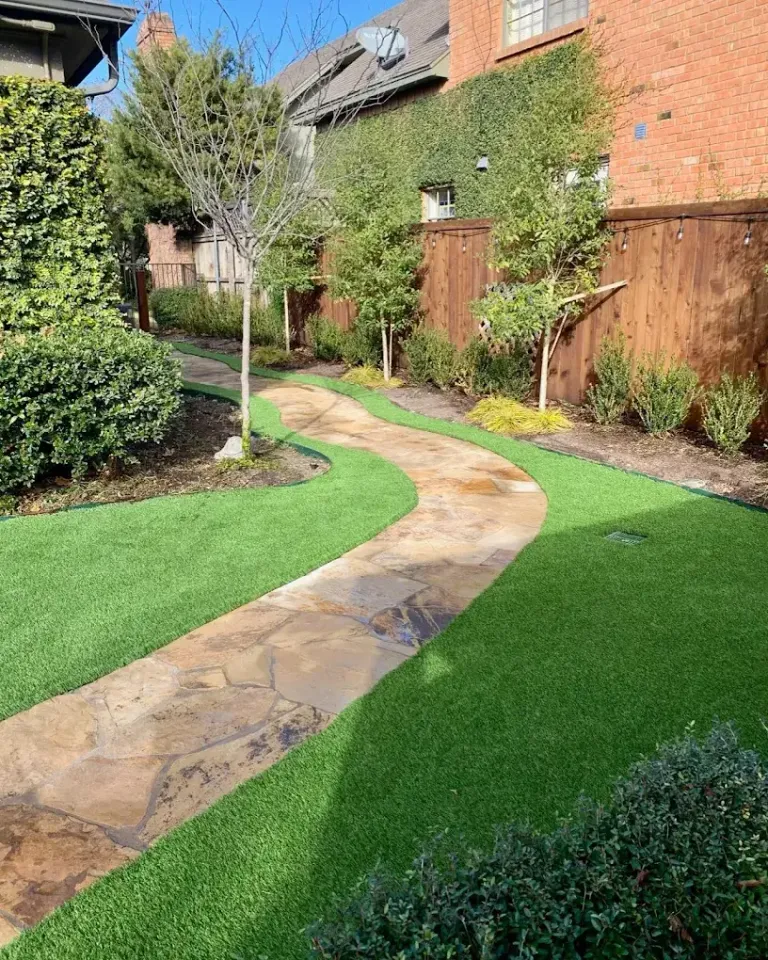 Synthetic turf on both sides of a flagstone garden path beside a wood fence