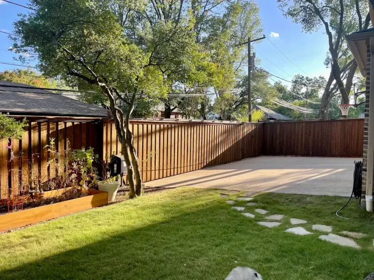 Stained board-on-board fence around a backyard with a concrete patio and stepping stones