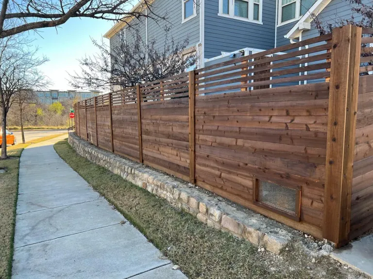 Horizontal cedar fence built on a low stone retaining wall along a sidewalk