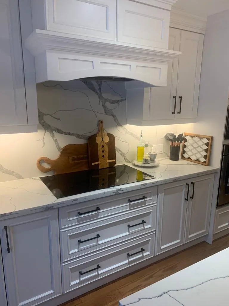 Custom white range hood with marble-look backsplash and shaker drawers