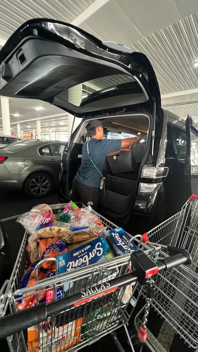 A trolley loaded with groceries next to the car boot
