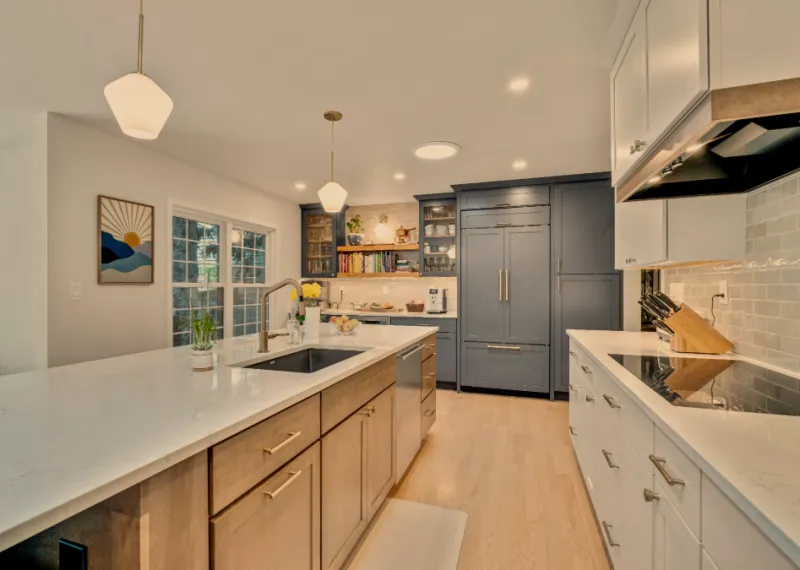 Two-tone kitchen remodel with navy cabinetry, white shaker island, quartz counters, and gold pendant lighting by CTC
