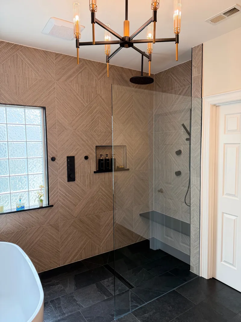 Frameless shower with geometric textured tile, matte-black fixtures and bench