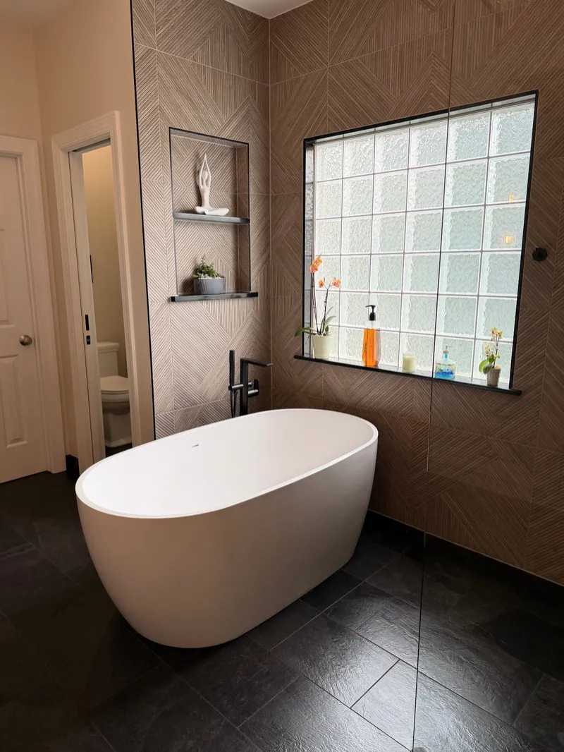 Freestanding bathtub against geometric feature tile with a black floor-mounted tub filler