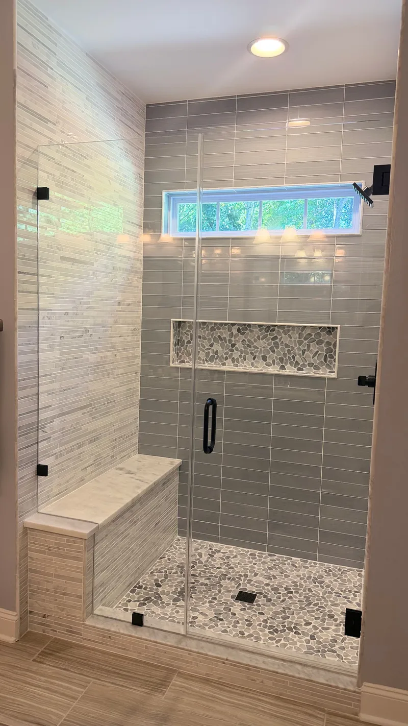 Glass shower enclosure with gray tile, pebble floor, niche and marble bench
