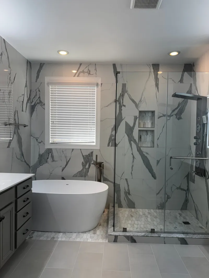 Freestanding bathtub beside a glass shower with veined tile walls and recessed niches