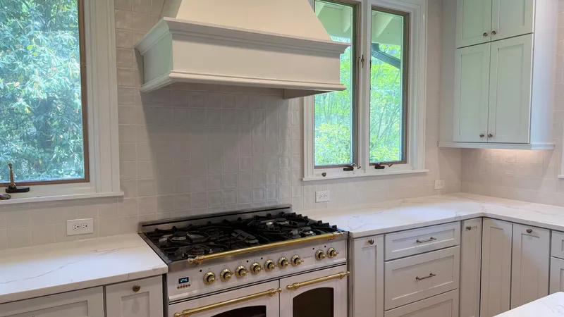 White kitchen with stone counters, cabinetry, range hood and white-and-gold range