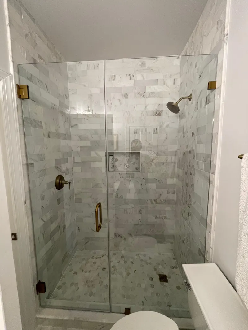 Frameless shower with marble-look wall tile, brass fixtures and hexagonal mosaic floor