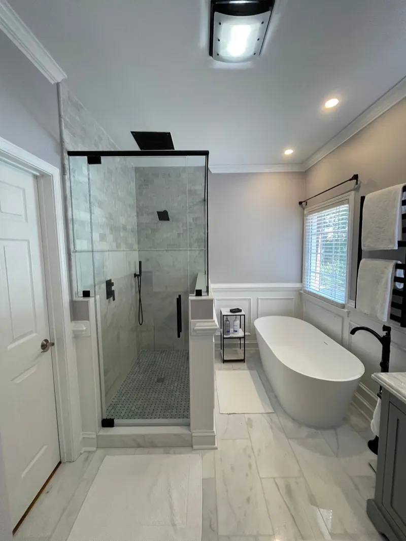 Freestanding bathtub and frameless shower with black hardware in a bright bathroom
