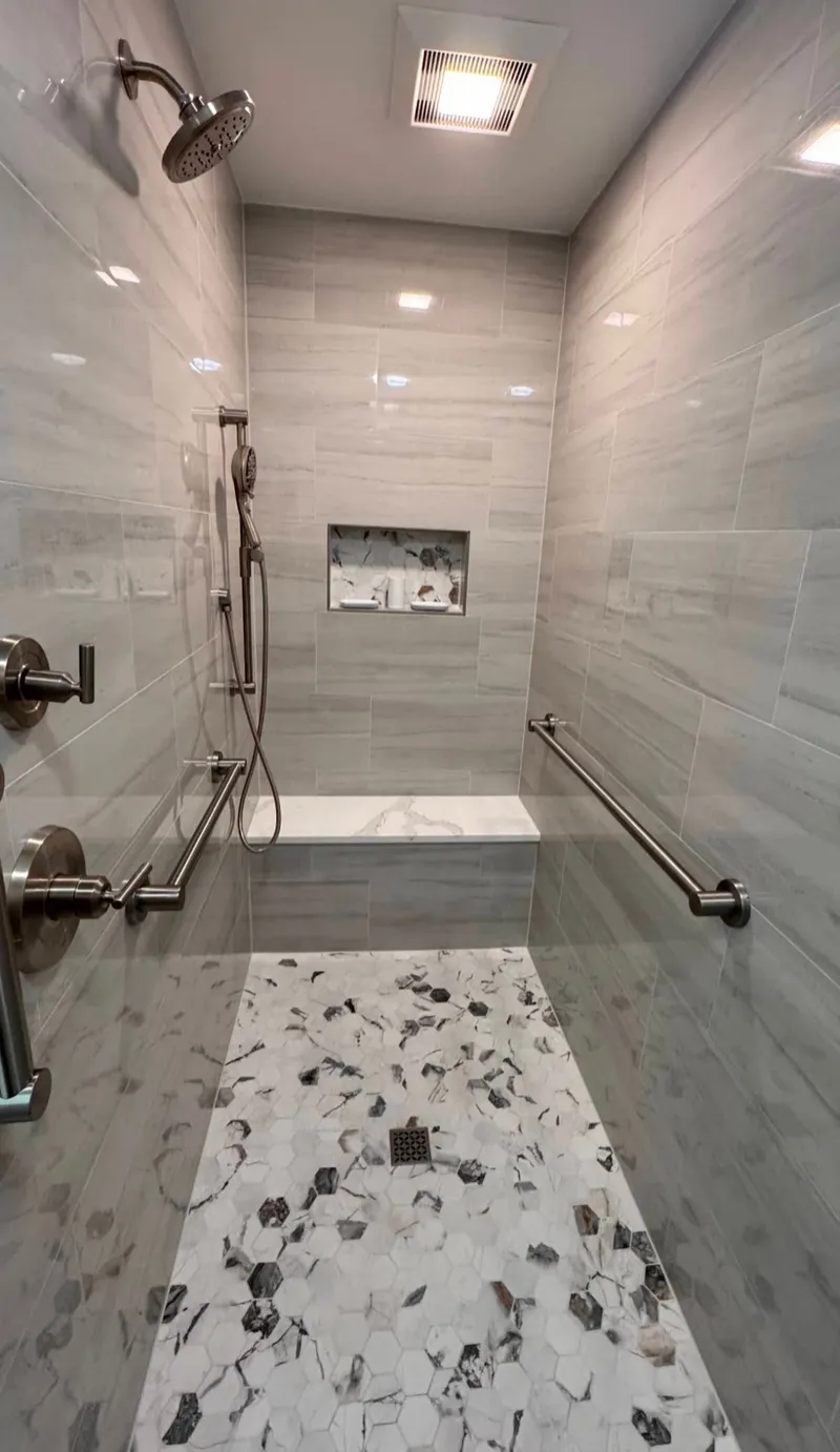 Gray-tiled shower with a built-in bench, grab bars, handheld shower and mosaic floor