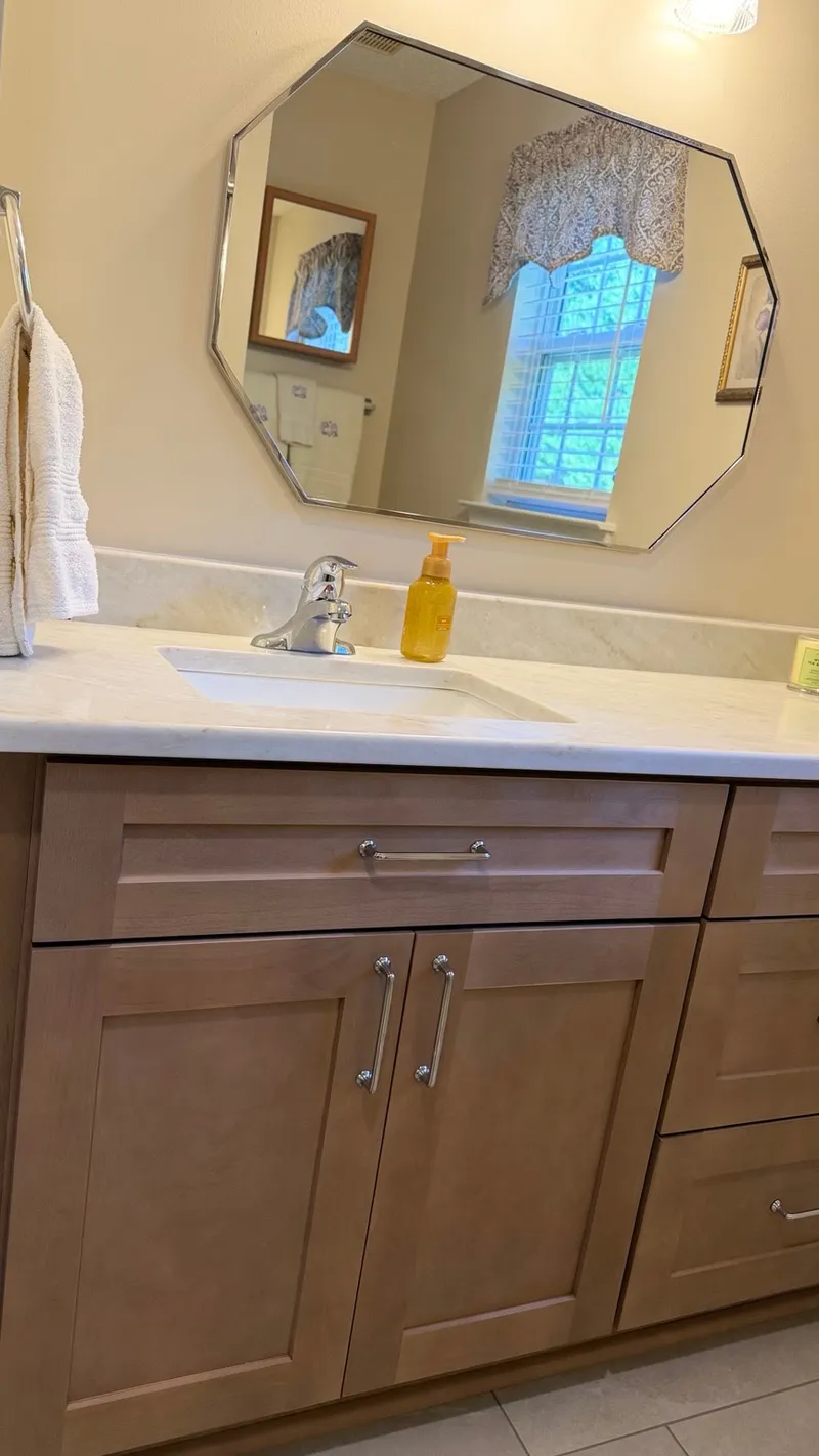 Wood bathroom vanity with a light countertop, chrome faucet and octagonal mirror