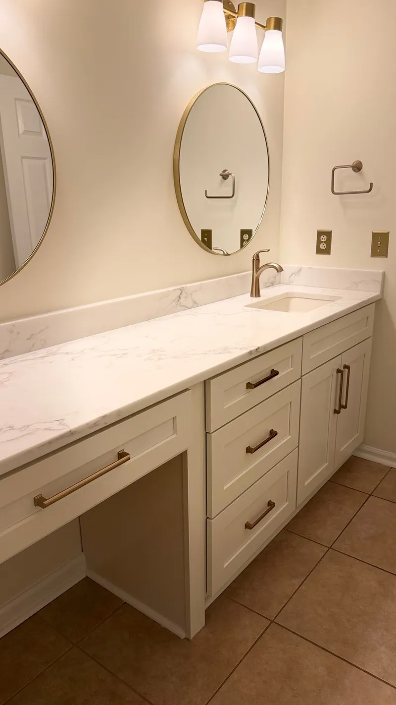 White double vanity with veined countertop, brass faucets and oval mirrors