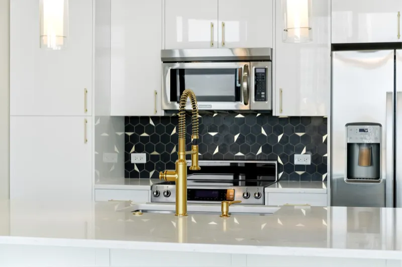 Full kitchen with quartz island, gold pre-rinse faucet, glass pendants and floor-to-ceiling white gloss cabinetry
