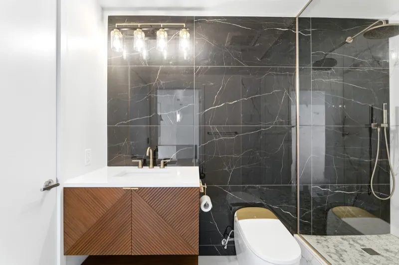 Front view of a floating chevron-pattern wood vanity with white quartz top, gold faucet and glossy black marble backsplash