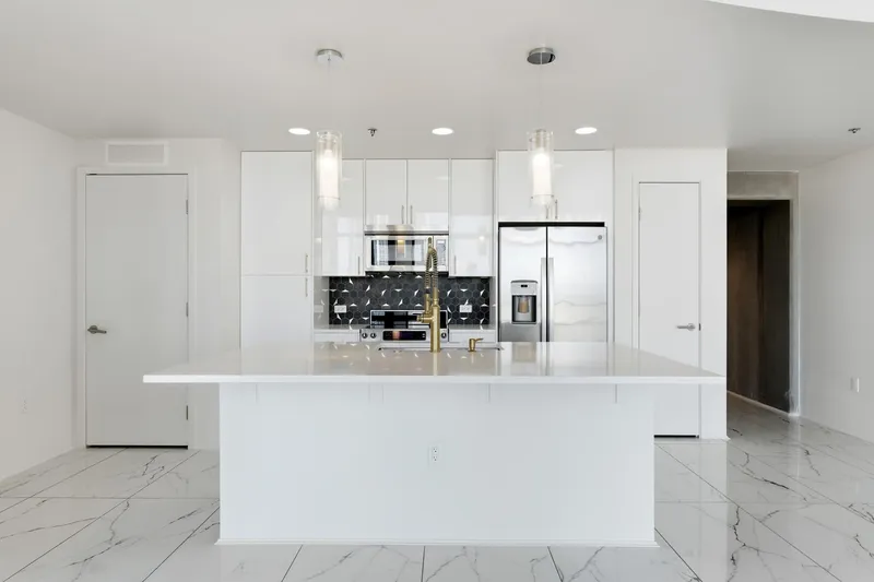 High-gloss white flat-panel kitchen with quartz island, charcoal hexagonal backsplash, gold hardware and glass pendant lights