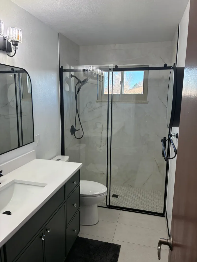 Full bathroom with charcoal vanity, marble walk-in shower with black hardware and arched mirror