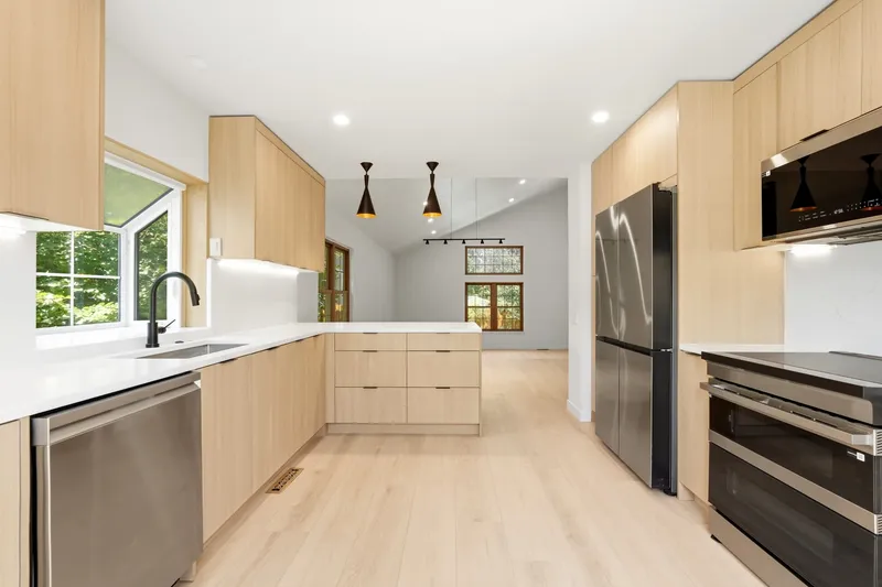 White oak flat-panel kitchen with quartz waterfall peninsula and black pendant lights
