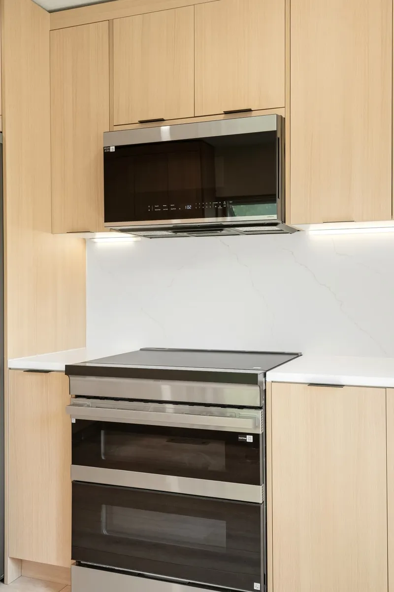 White oak cabinetry with slab quartz backsplash, stainless double oven range and integrated microwave hood