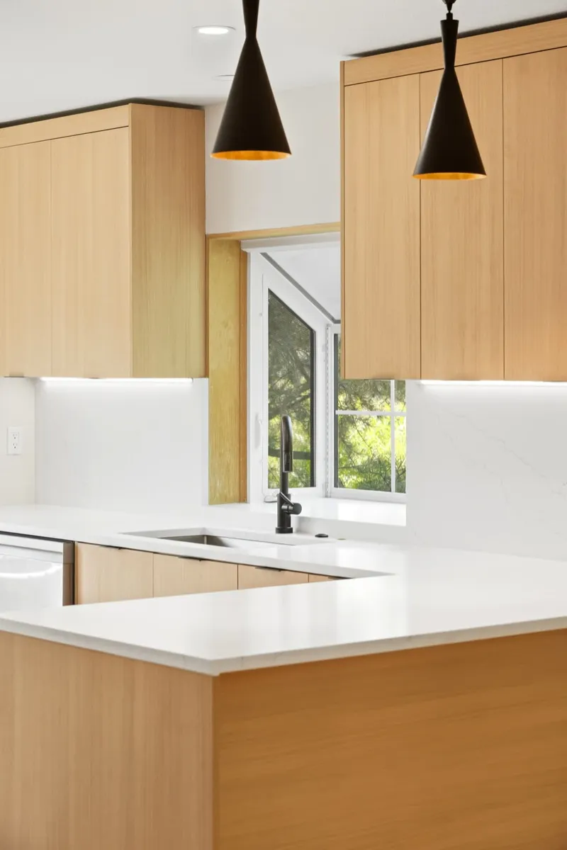 Full-height oak cabinetry with black cone pendants over a quartz peninsula