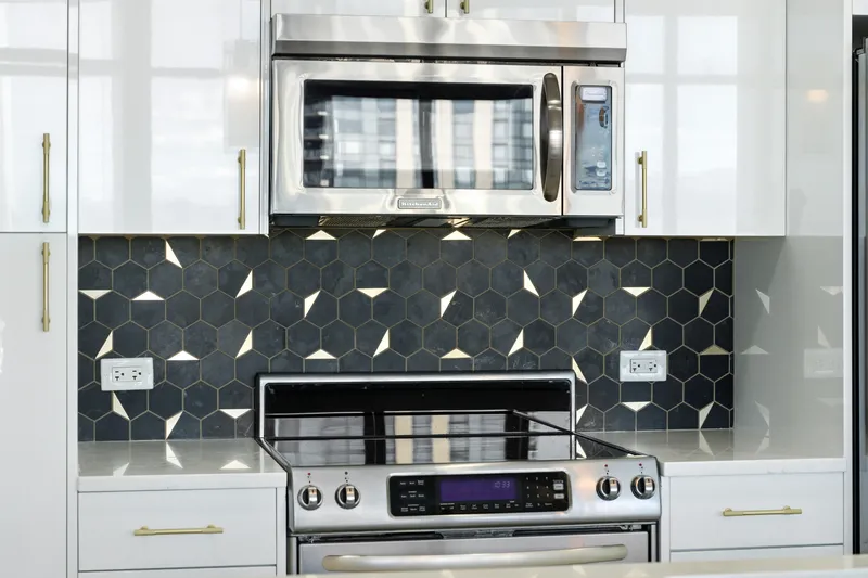 Black and white hex tile backsplash behind a stainless range with gold cabinet pulls