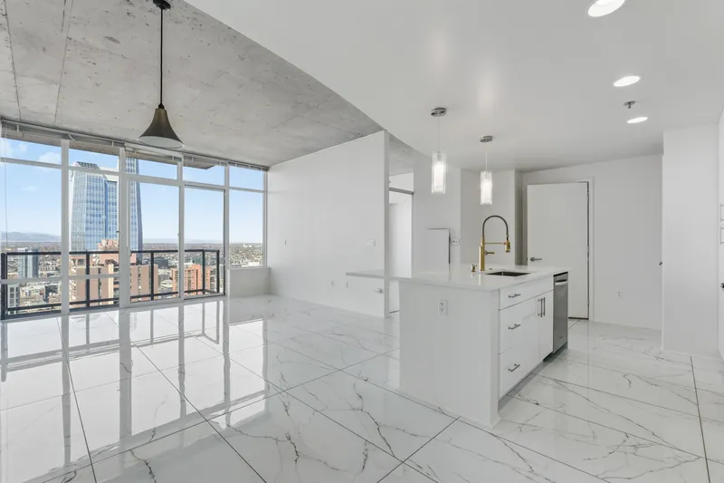Condo kitchen island with gold faucet beside floor-to-ceiling windows and marble-look tile floors