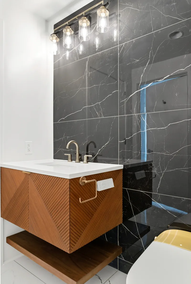 Floating chevron wood vanity with black marble wall and gold vanity light