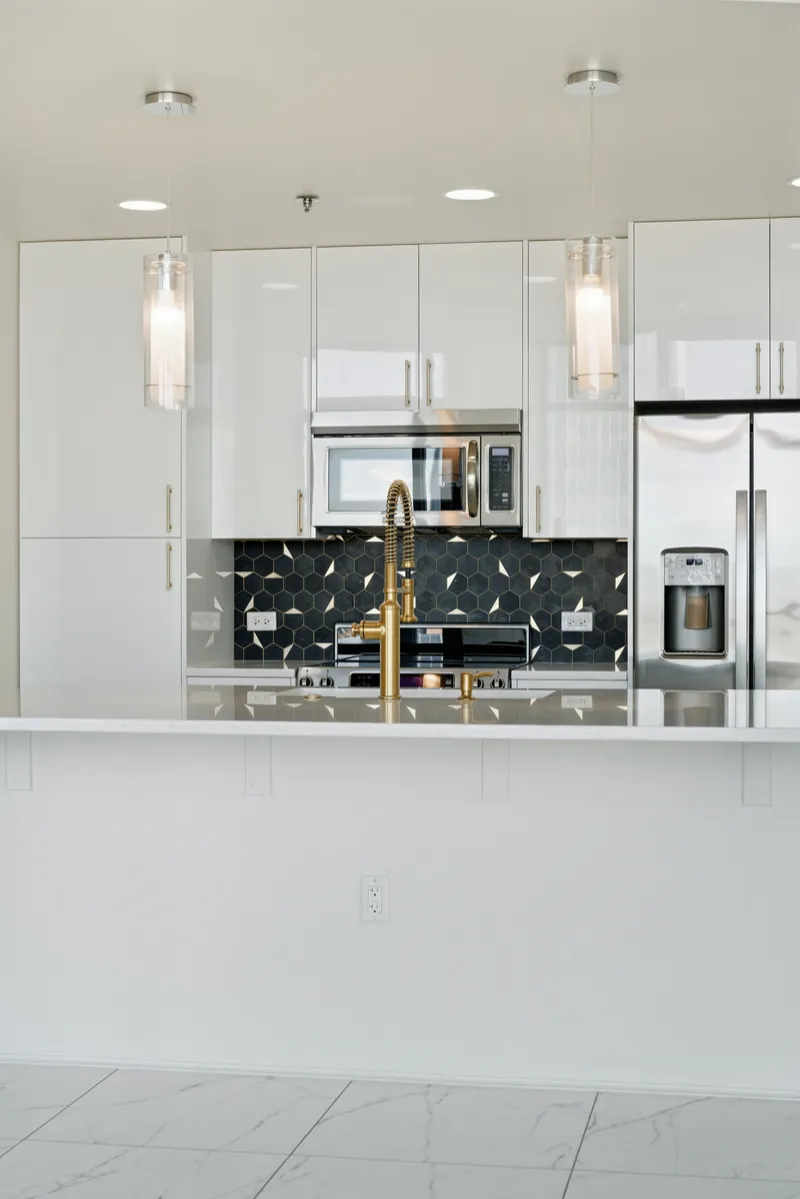 White gloss condo kitchen with quartz island, glass pendants and stainless appliances