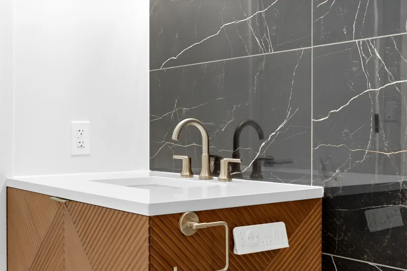 Brushed gold faucet on a chevron wood vanity against glossy black marble tile