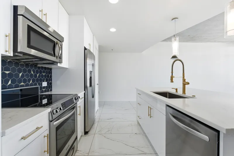 High-rise kitchen with white gloss cabinetry, black hex tile backsplash, gold faucet and city views