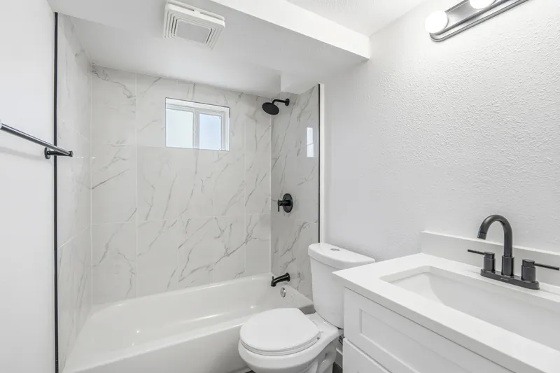 Tub and shower with marble-look surround, matte black fixtures and white vanity