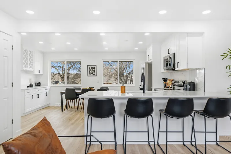 Open white shaker kitchen with quartz peninsula and black counter stools