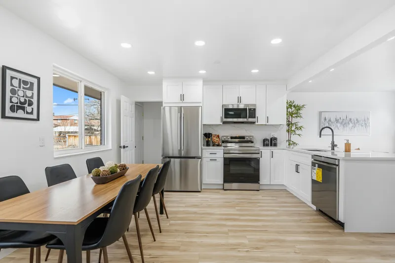 White shaker kitchen with stainless appliances opening to a dining area with luxury vinyl plank floors